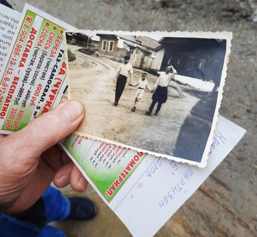 Пенсионер показывает фотографию, где видно, какой высокой была дорога на пересечении улиц Свердлова и Красных Партизан, когда он 10- летним мальчишкой бегал в библиотеку на углу улицы.