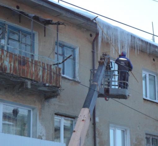 С помощью специального резака рабочий срубает сосульки с крыш жилых домов.