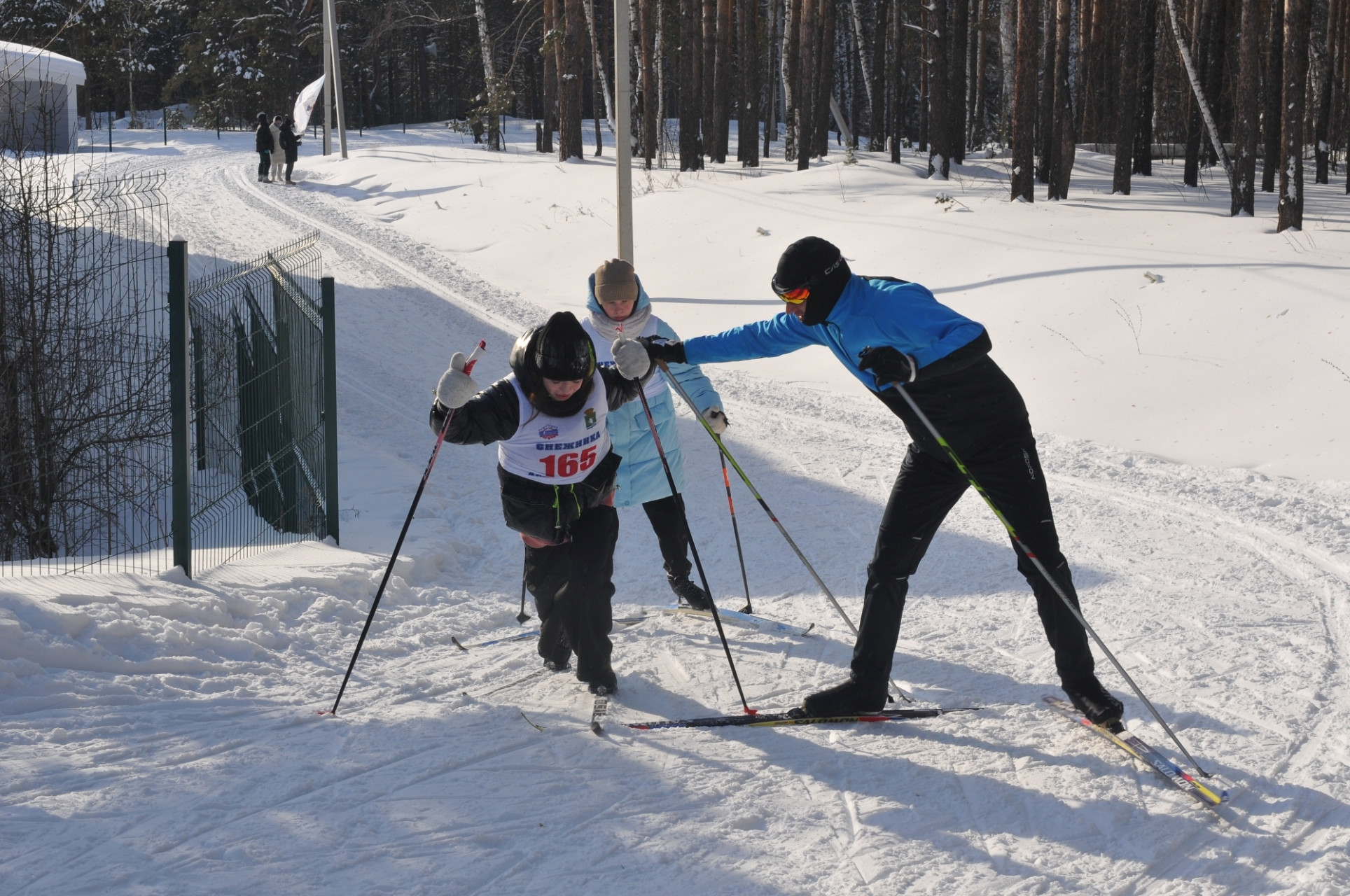 На самом крутом подъеме трассы профессиональный лыжник, не участвующий в забегах, помогает малоопытной молодежи. Похвально.